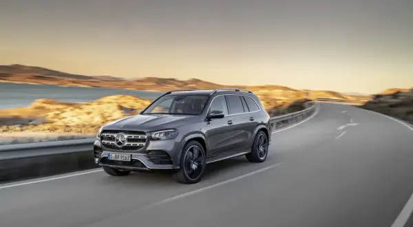 Szary Mercedes GLS 580 sunie po krętej drodze nad brzegiem morza podczas zachodu słońca.