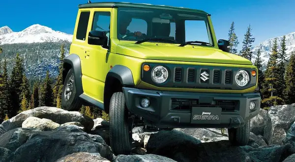 Żółty Suzuki Jimny 2026 pokonuje skalisty teren, gotowy na przygodę w górach.