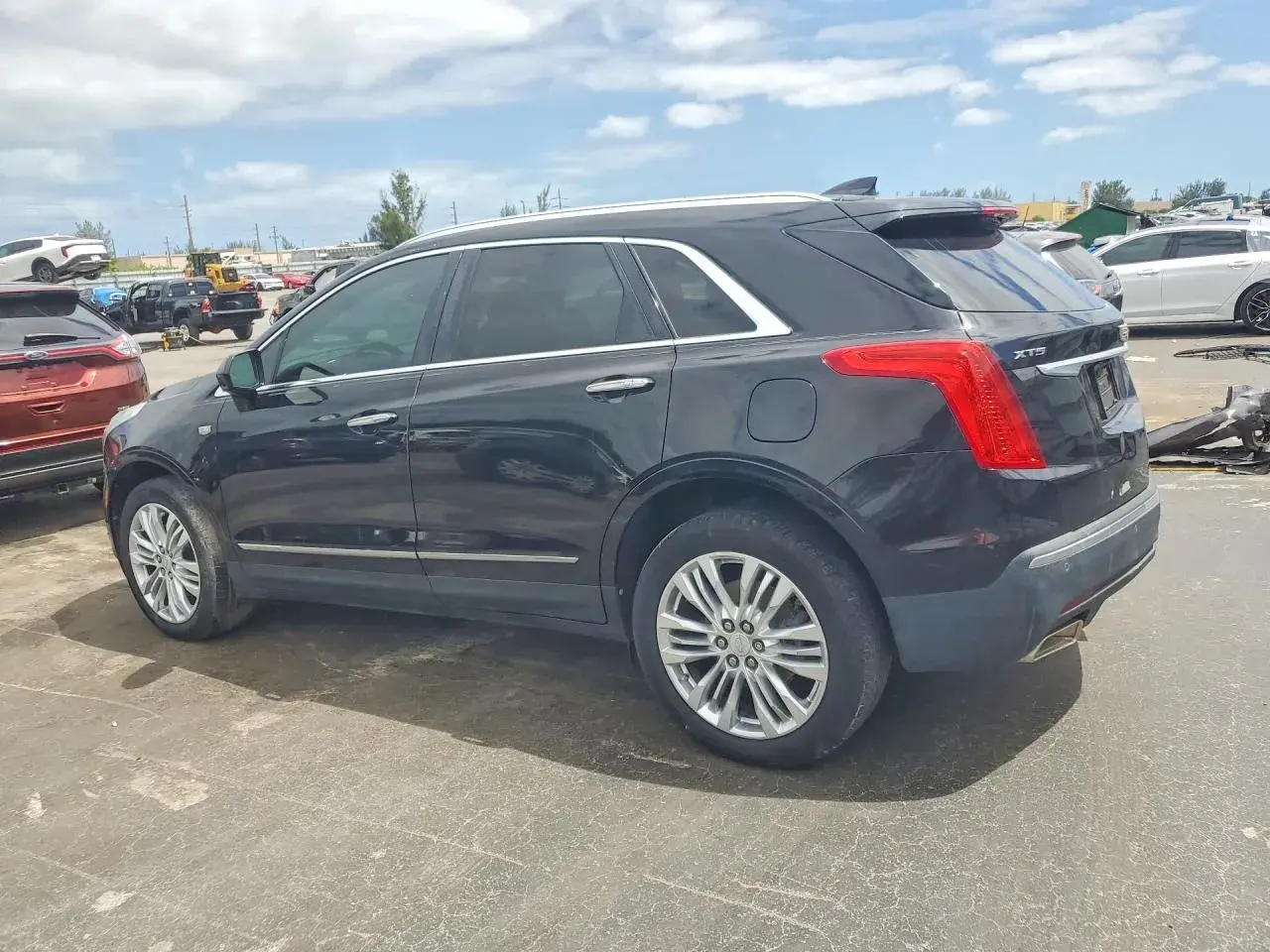 Czarny Cadillac XT5 stoi na placu wśród innych pojazdów.