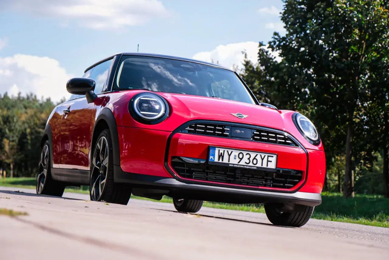 Czerwony Mini Cooper na tle zieleni. Wiele osób szuka opinii o tym modelu, a ten egzemplarz wygląda na gotowy do jazdy.