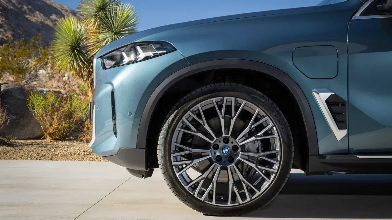 Nowe BMW X5 2023 w kolorze niebiesko-zielonym, z felgami o skomplikowanym wzorze, zaparkowane na tle pustynnego krajobrazu.