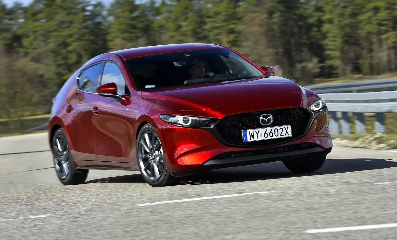 Czerwona Mazda 3 2025 na drodze, z widocznym kierowcą.