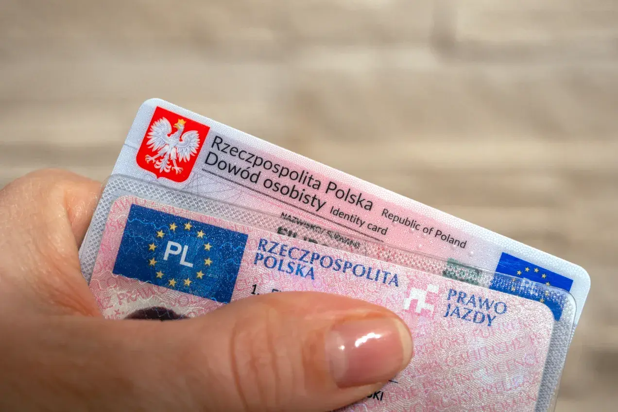 Dłoń trzyma polski dowód osobisty i prawo jazdy. To ważne dokumenty, które pozwalają na legalne poruszanie się po drogach, a niektóre z nich, jak prawo jazdy bezterminowe, są ważne przez całe życie.