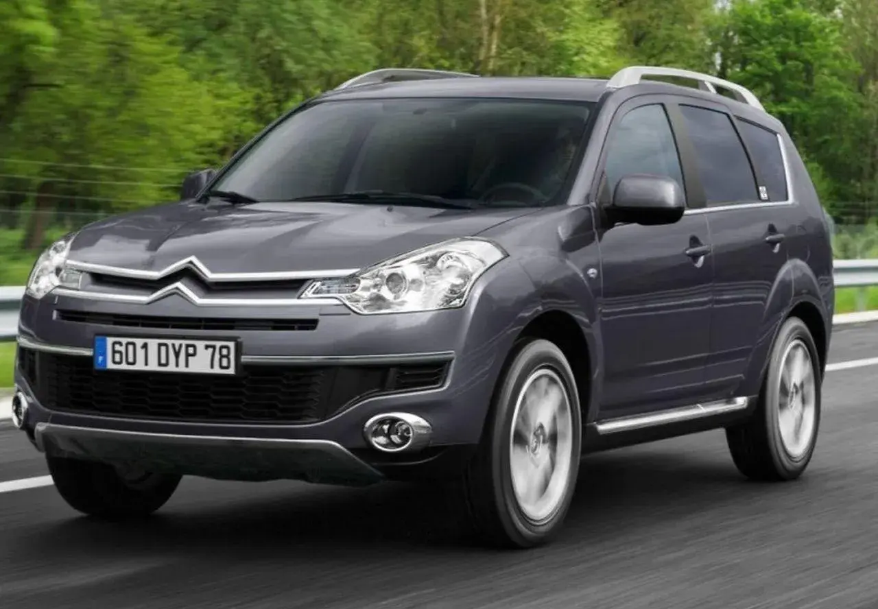 Szary Citroen C-Crosser jedzie po drodze, otoczony zielenią.