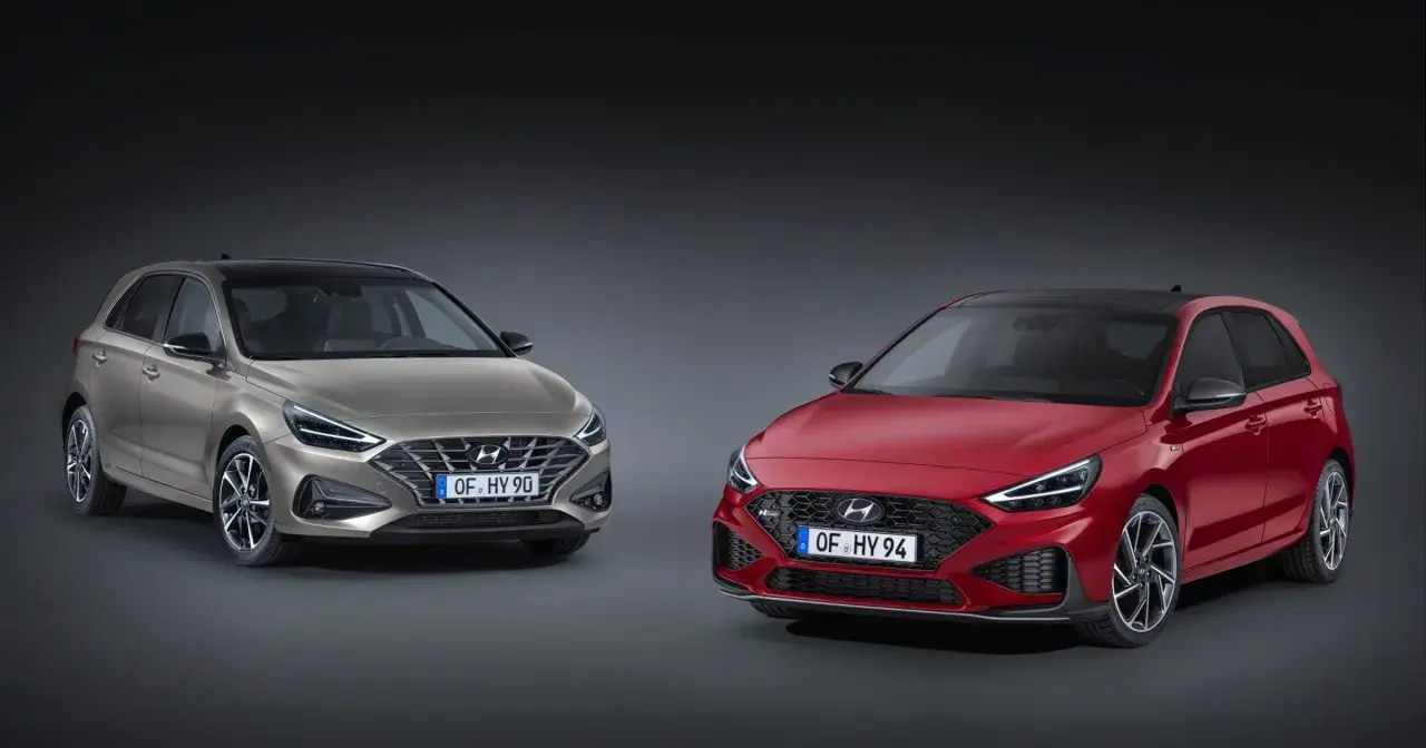Dwa modele Hyundai i30 2024: jeden w kolorze złotym, drugi w czerwonym, prezentują nowoczesny design i sportowe linie.