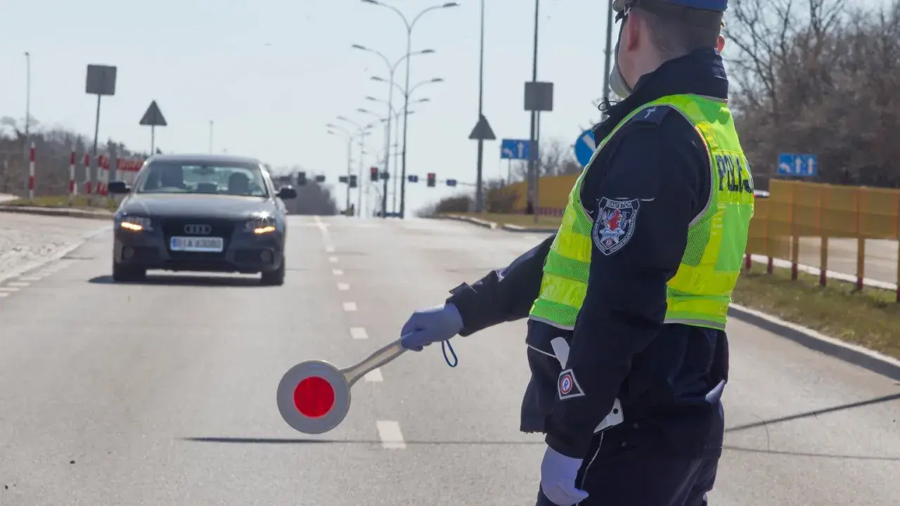 Policjant kieruje ruchem, zatrzymując samochód. Może to być kontrola drogowa lub kurs reedukacyjny.