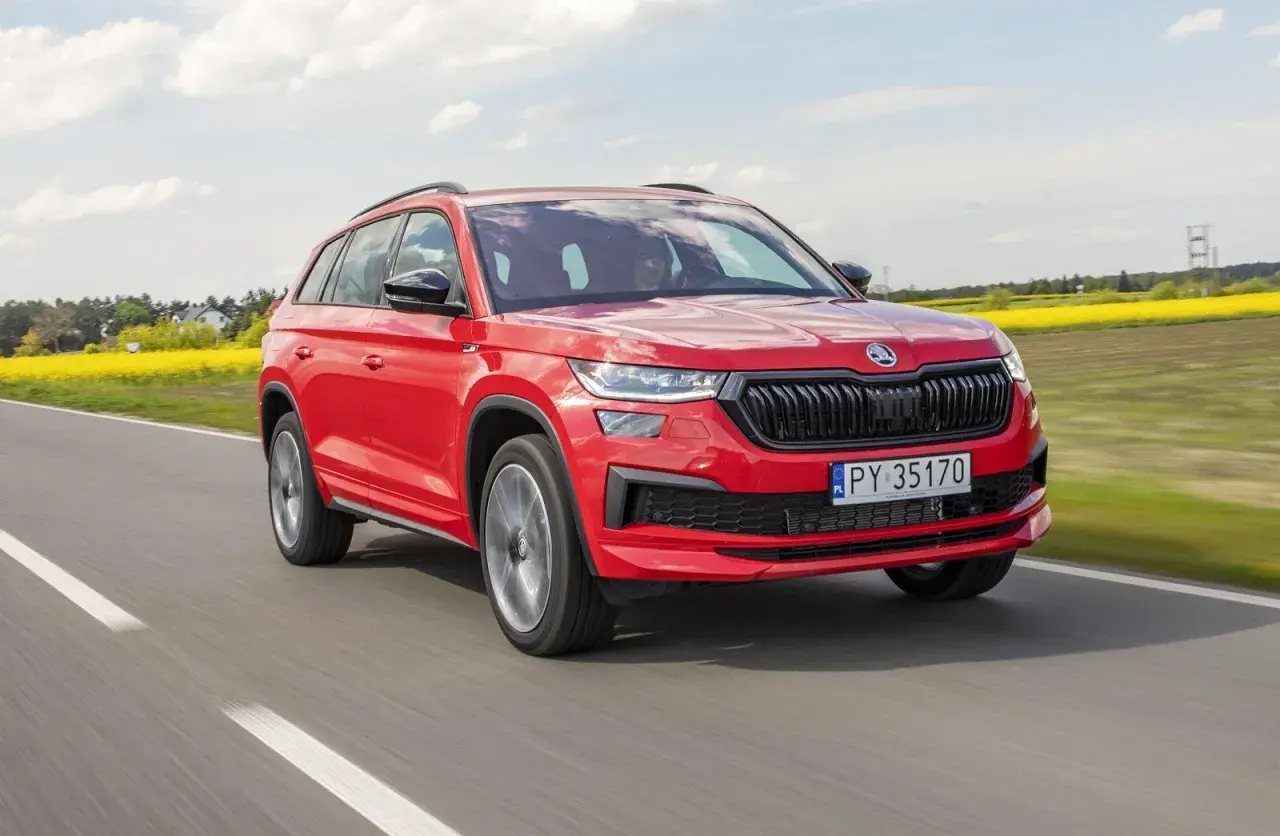 Czerwony Skoda Kodiaq 2023 pędzi po drodze, mijając kwitnące pola rzepaku.