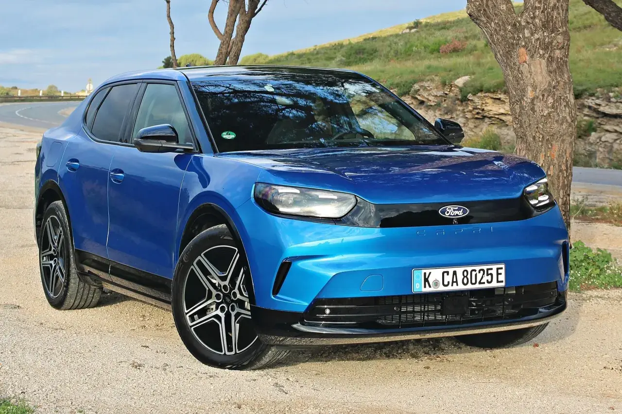 Niebieski Ford Capri 2025, nowoczesny elektryczny SUV, zaparkowany na żwirowej drodze obok drzewa.