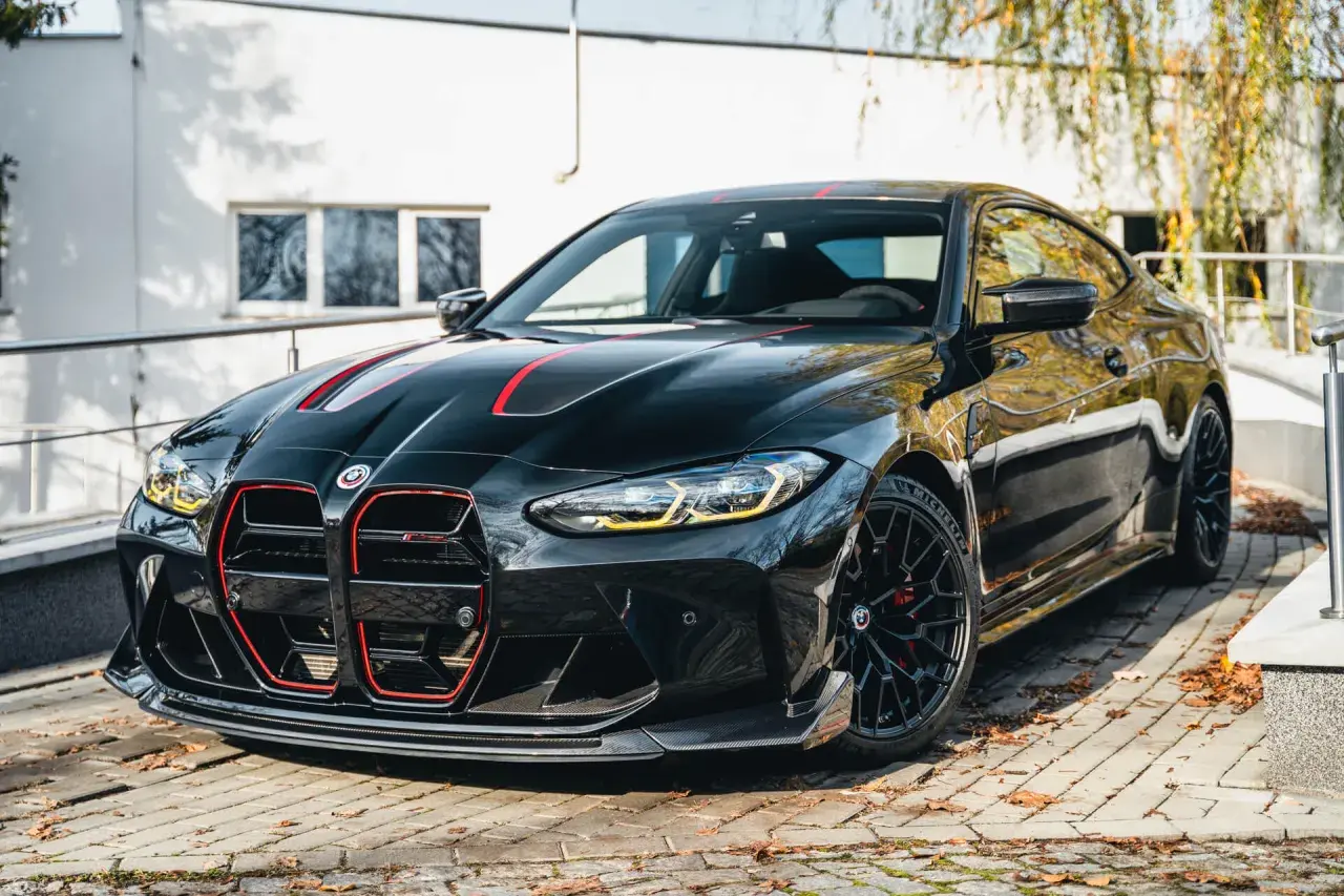 Czarny BMW M4 CSL z czerwonymi akcentami na masce i grillu, zaparkowany na brukowanej nawierzchni.
