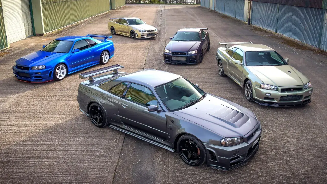 Pięć kultowych Nissanów GT-R R34 w różnych kolorach, stojących na betonowym placu.