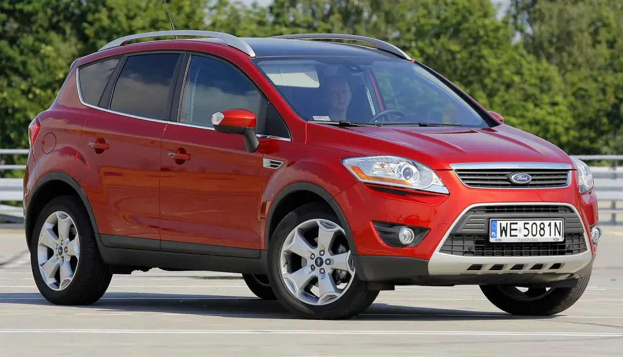 Czerwony Ford Kuga na parkingu. Kierowca w środku. Wiele osób szuka ford kuga opinie przed zakupem.