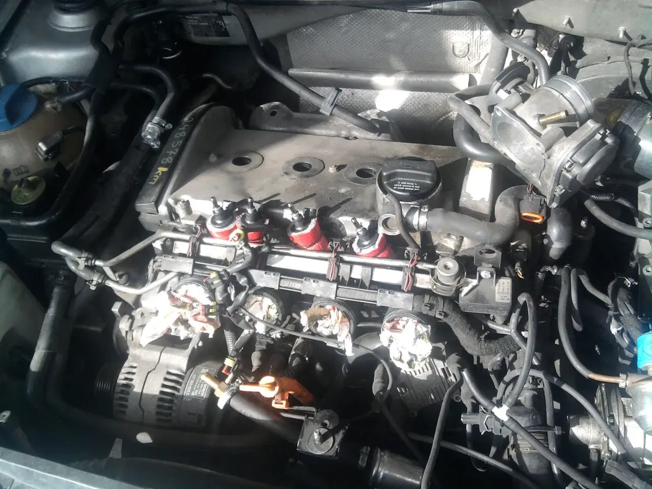 Silnik Audi A4 B6 2.0 benzyna w trakcie prac. Widoczne cewki zapłonowe, przepustnica i alternator.