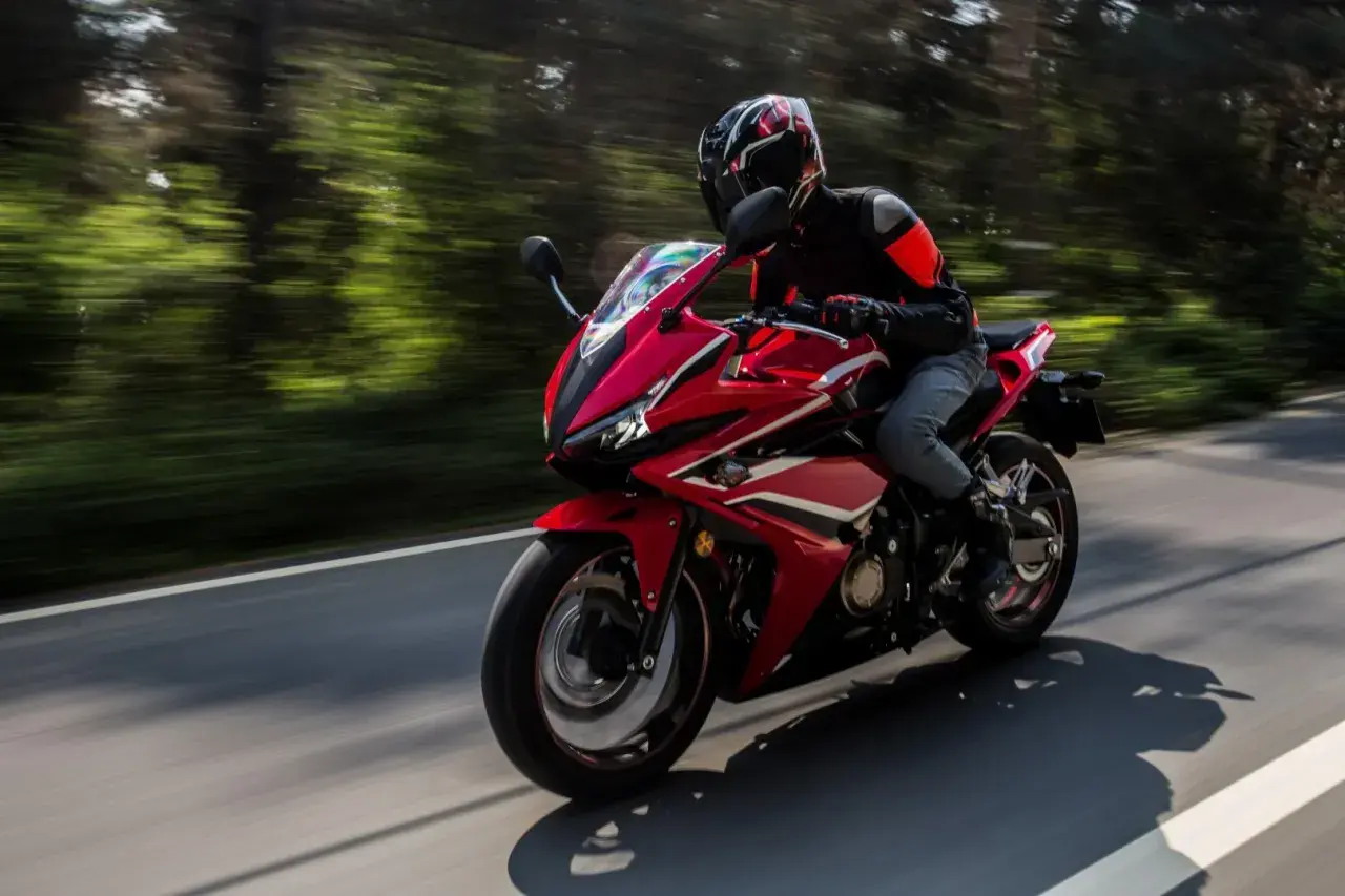 Motocyklista w kasku i kurtce jedzie sportowym, czerwonym motocyklem. Idealny sprzęt na pierwsze prawo jazdy a2.