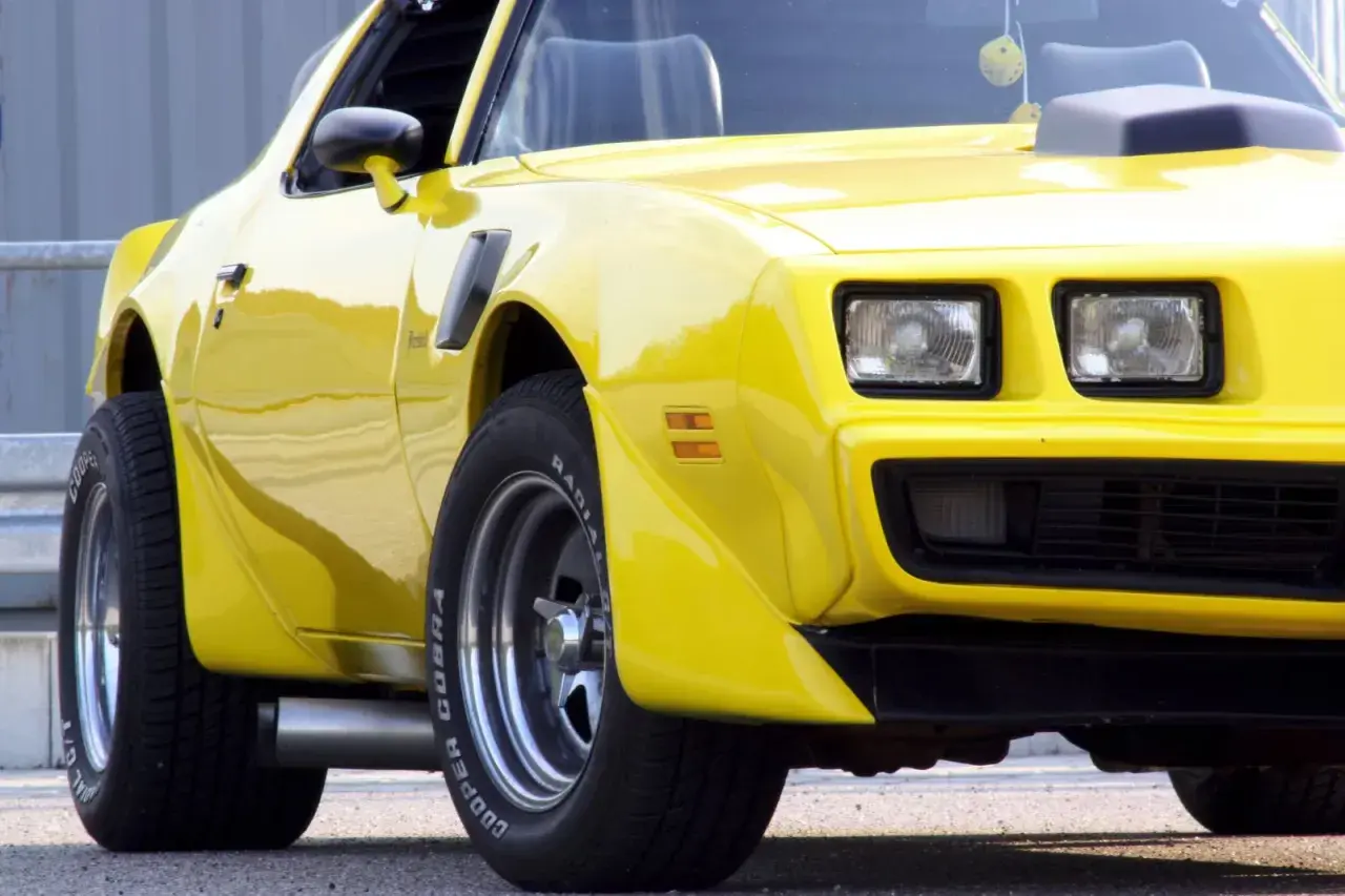 Żółty Pontiac Trans Am z lat 70. z charakterystycznym wlotem powietrza na masce i szerokimi oponami Cooper Cobra.