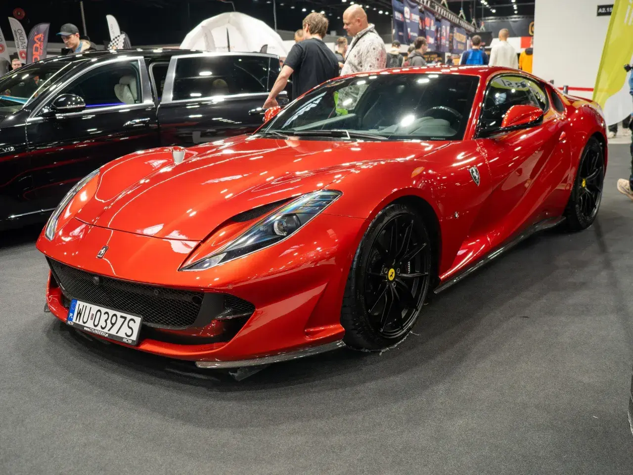 Błyszczący, czerwony Ferrari 812 Superfast z czarnymi felgami na wystawie motoryzacyjnej.