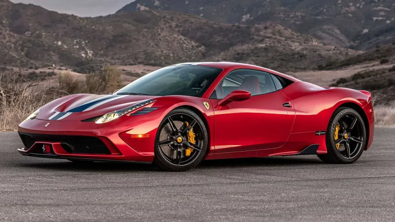 Czerwone Ferrari 458 z białymi i niebieskimi pasami na masce, zaparkowane na tle górskiego krajobrazu.