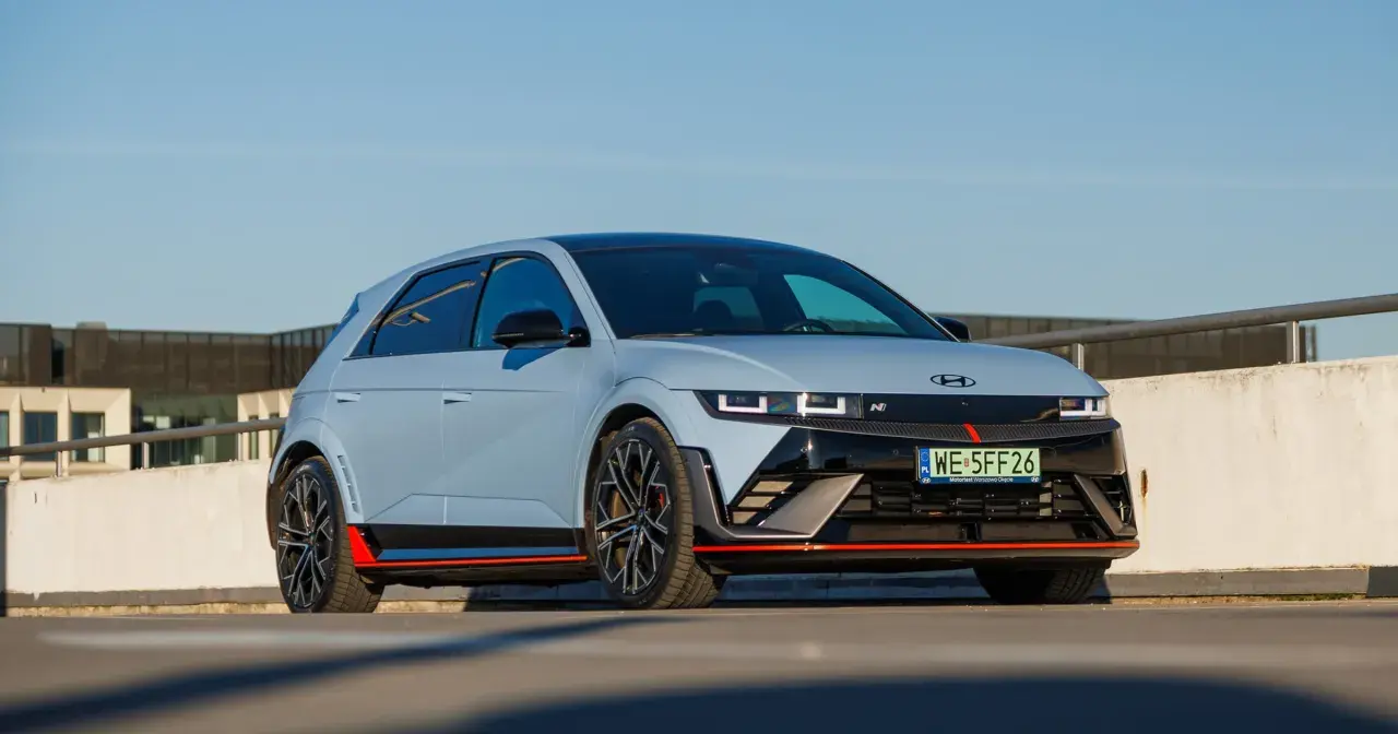 Sportowy Hyundai Ioniq 5 N z czerwonymi akcentami i czarnymi felgami na tle betonowego muru i błękitnego nieba.