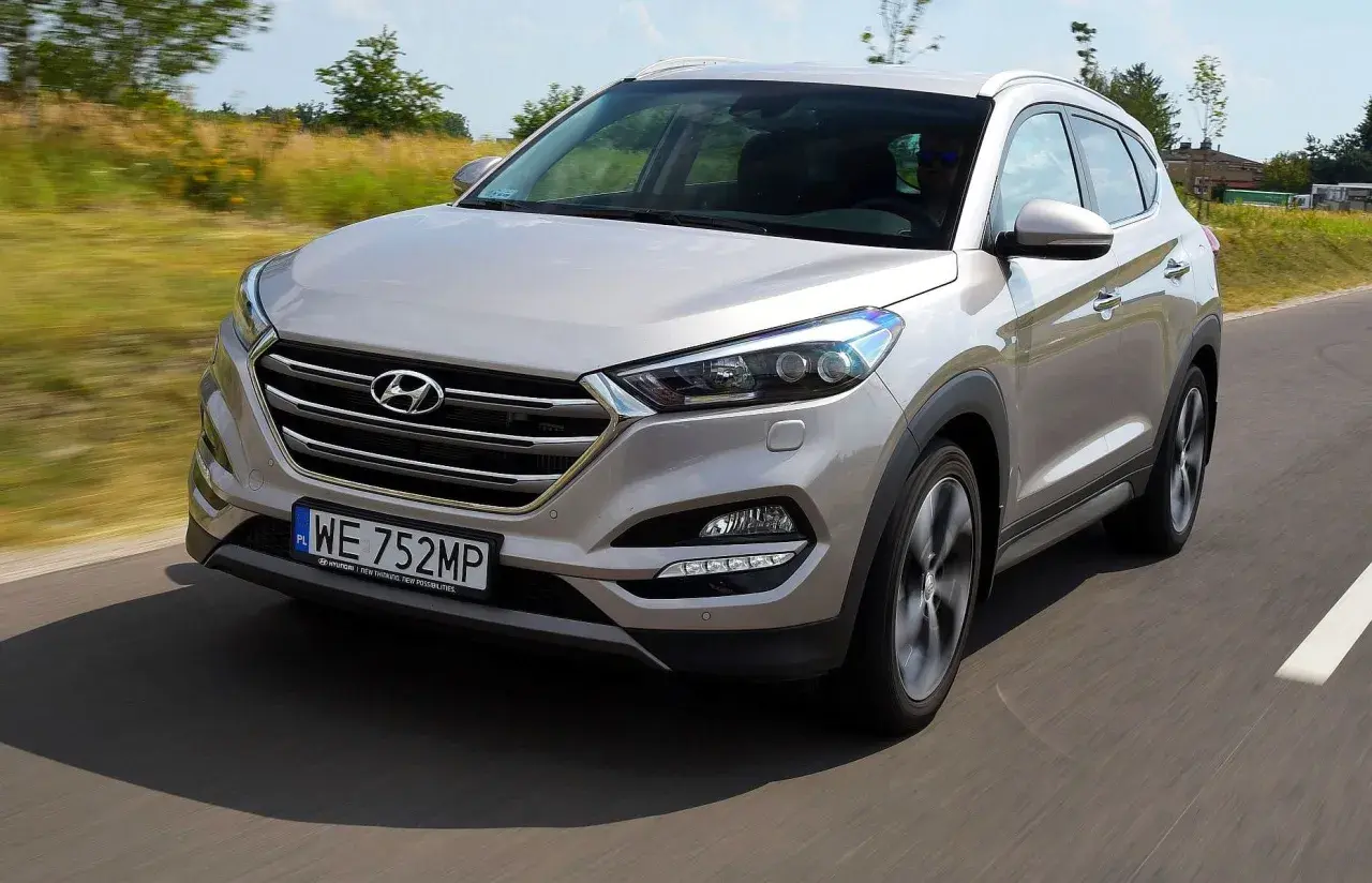 Srebrny Hyundai Tucson 2016 jedzie po drodze, otoczony zielenią.