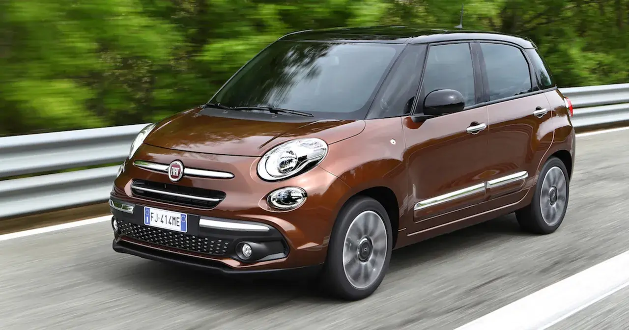 Brązowy Fiat 500L z czarnym dachem pędzi po drodze, otoczony zielenią.