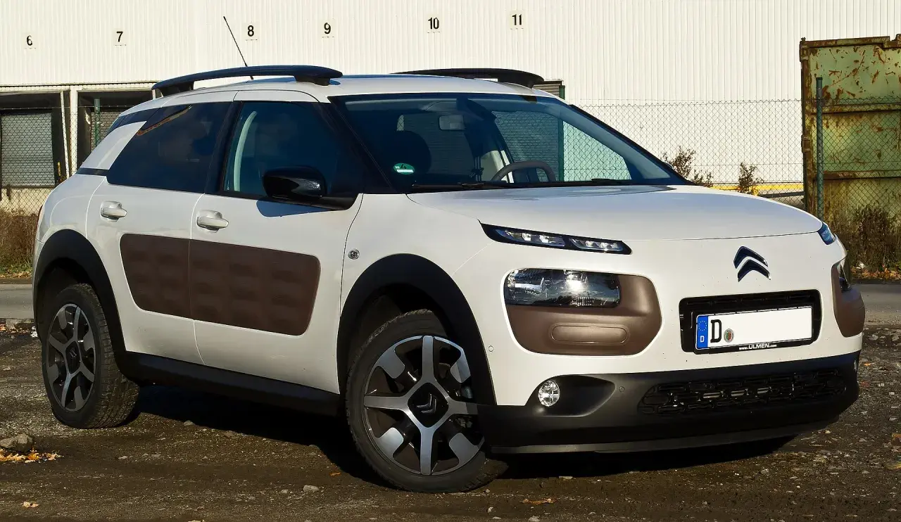 Biały Citroen Cactus z brązowymi wstawkami Airbump na drzwiach, zaparkowany na brudnym podjeździe.
