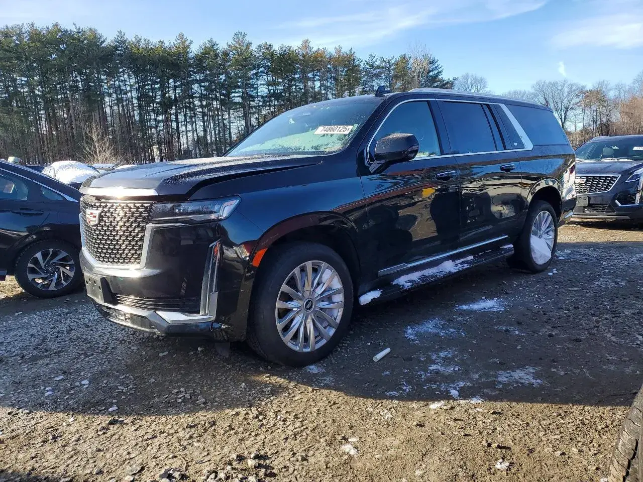Czarny Cadillac Escalade 2025 z chromowanymi felgami i detalami, zaparkowany na żwirowym placu z resztkami śniegu.