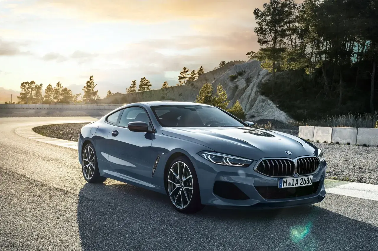 Szary BMW 840d na zakręcie toru wyścigowego, z drzewami i skalistym zboczem w tle.