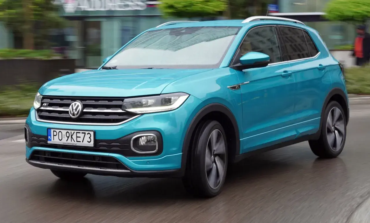 Turkusowy Volkswagen T-Cross w ruchu miejskim, z widocznym numerem rejestracyjnym PO 9KE73.