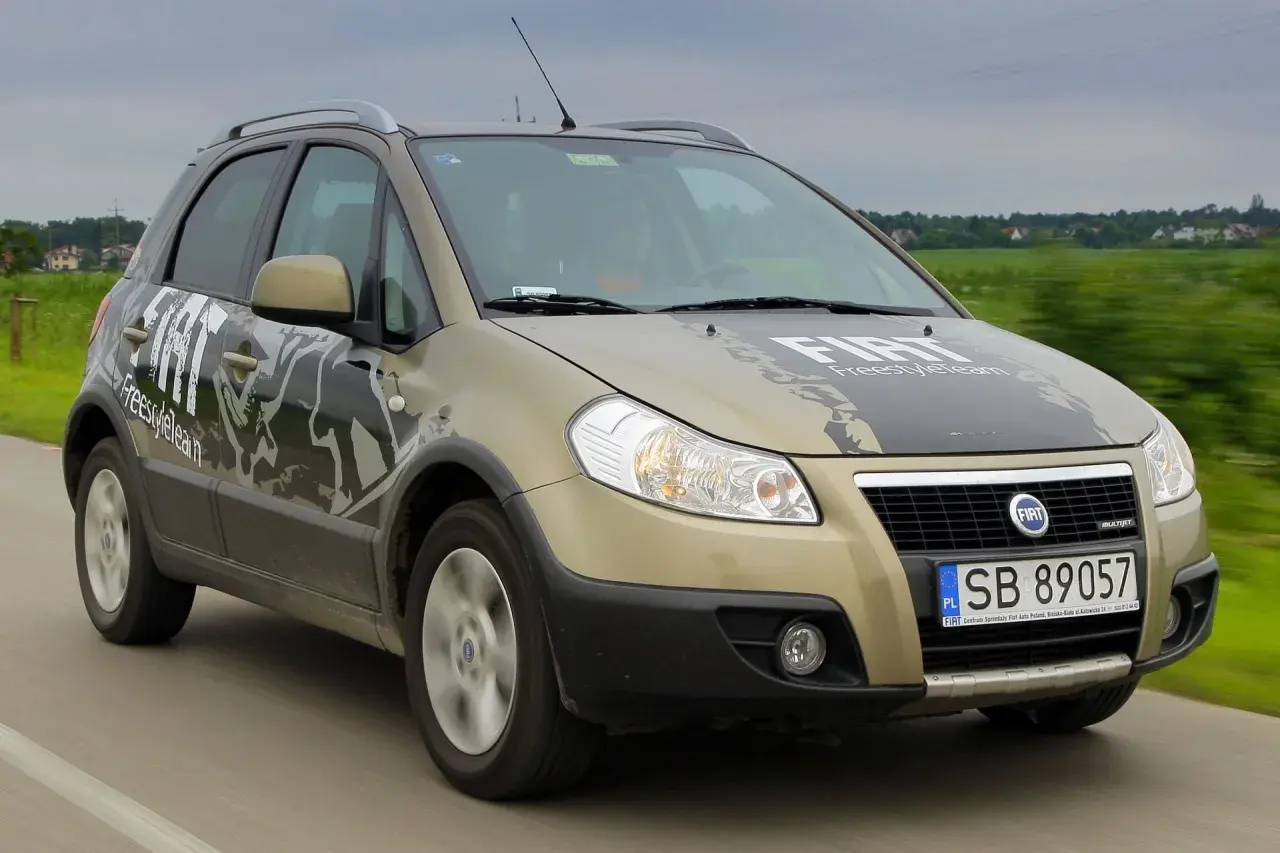 Złoty Fiat Sedici z napisem "FreestyleTeam" na masce i drzwiach jedzie po drodze.