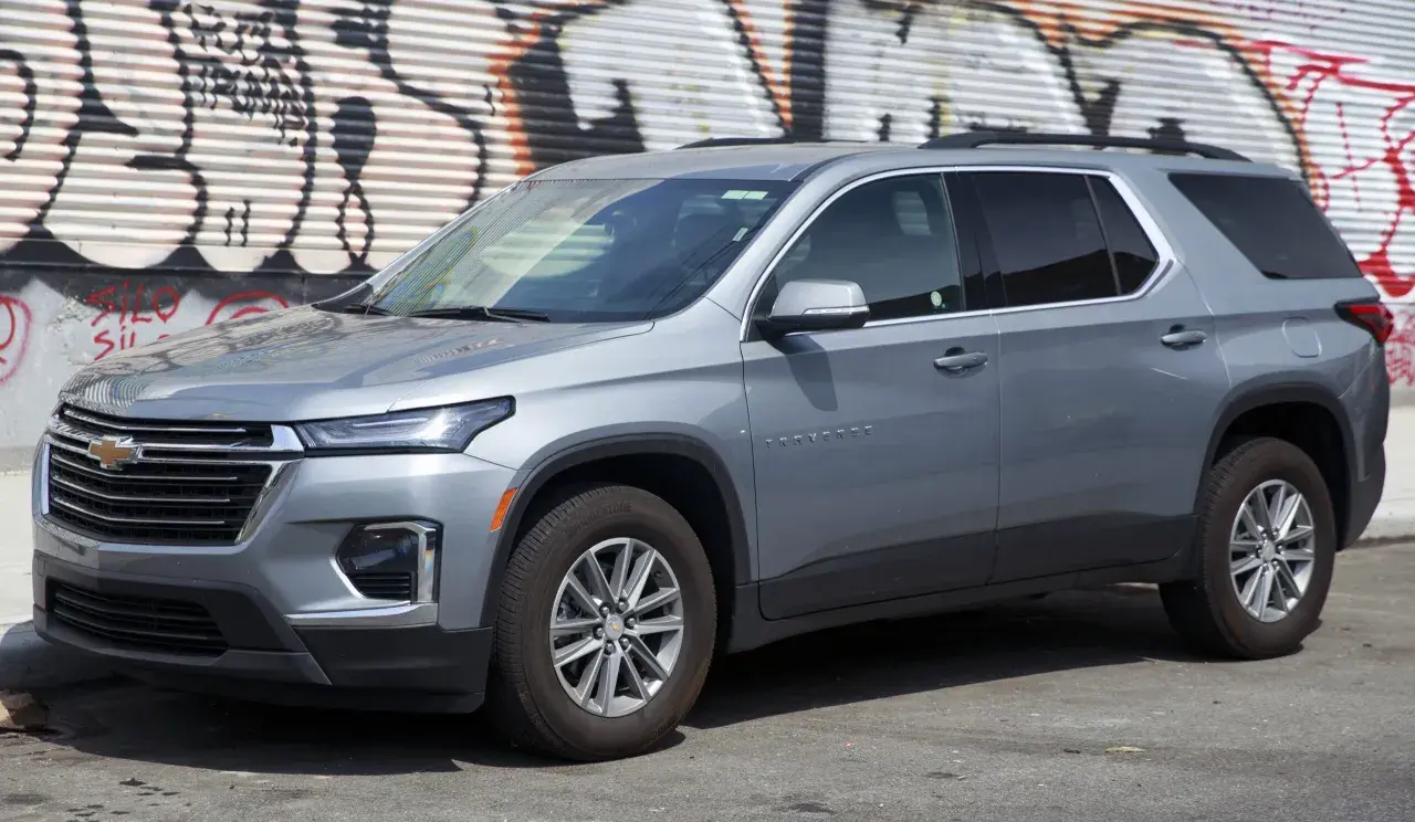 Szary Chevrolet Traverse SUV zaparkowany przed ścianą z graffiti.