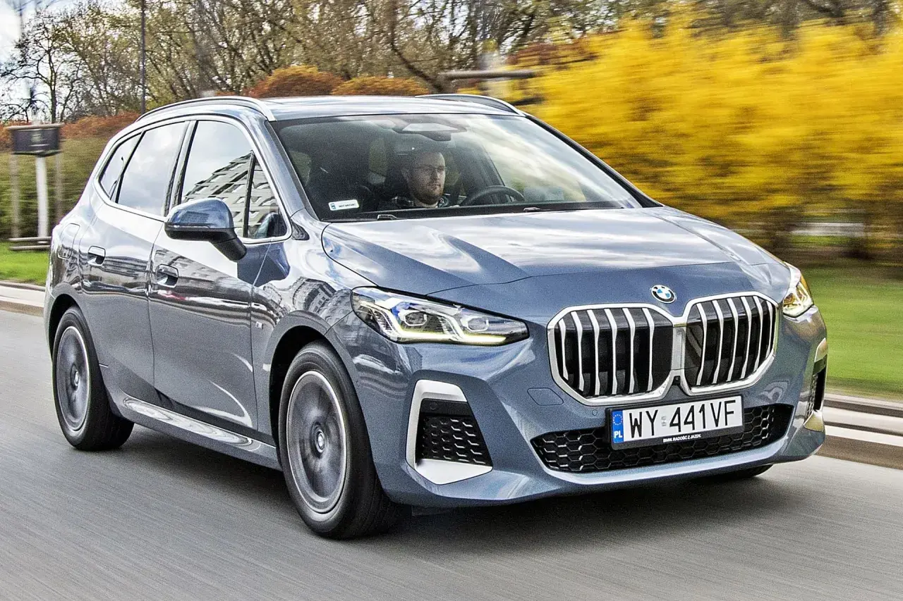 Szary BMW 2 Active Tourer jedzie po drodze, za nim widać żółte krzewy.