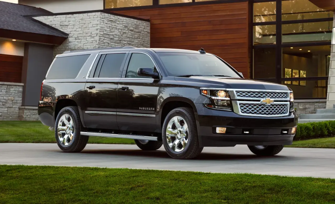 Czarny Chevrolet Suburban na podjeździe przed nowoczesnym, podmiejskim domem z kamiennymi i drewnianymi elementami.
