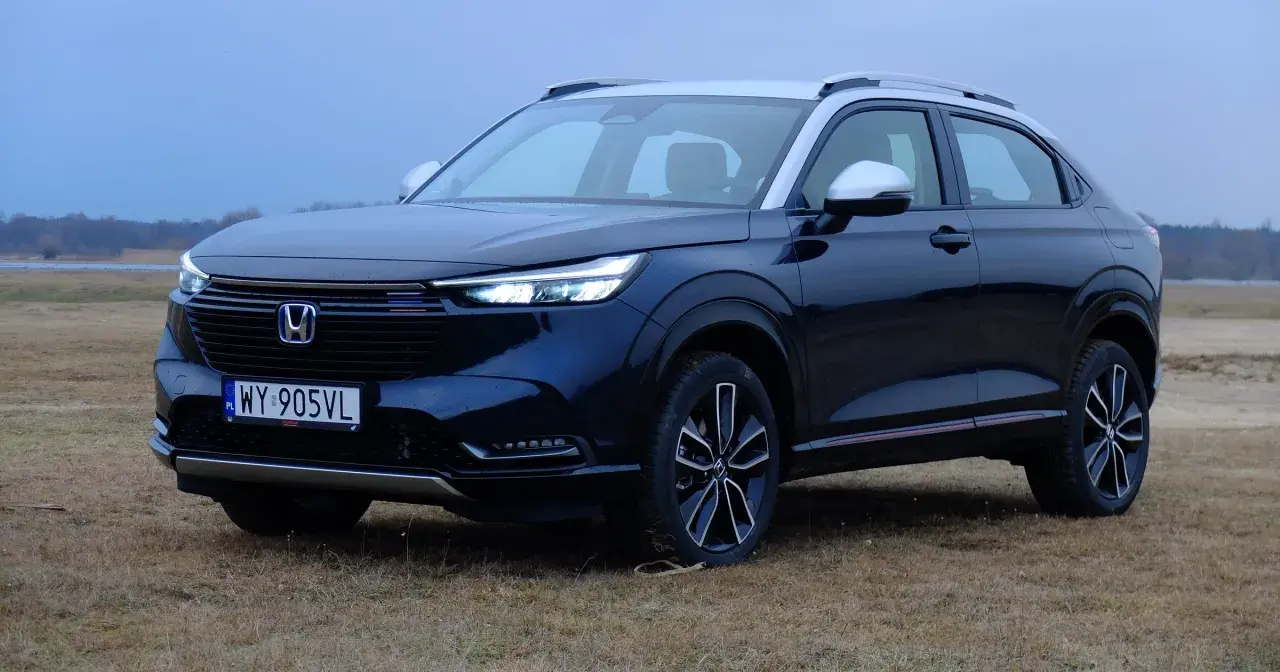 Ciemnogranatowa honda hybryda z srebrnym dachem i lusterkami, zaparkowana na trawiastym polu.