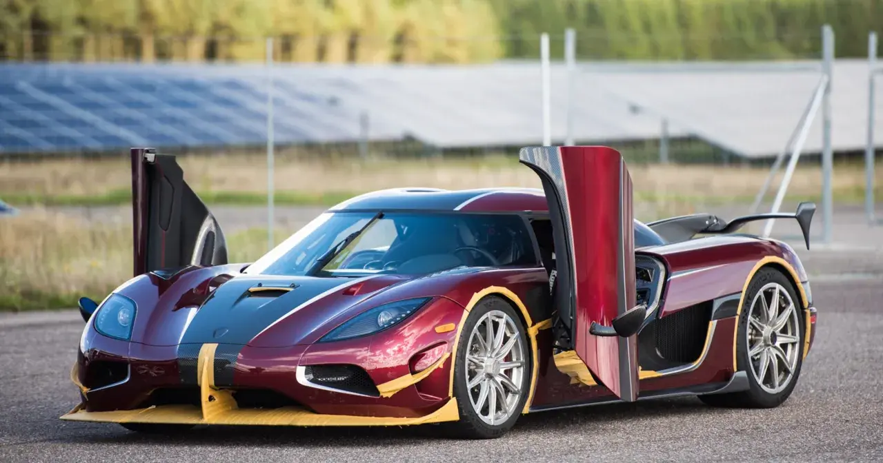 Czerwony Koenigsegg Agera RS z otwartymi drzwiami, gotowy do startu na tle paneli słonecznych.