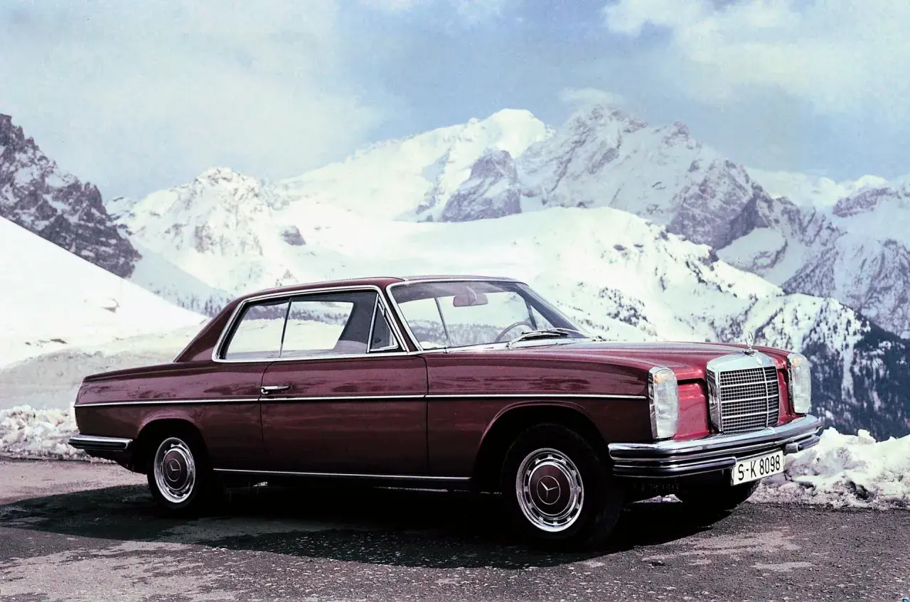 Ciemnoczerwony Mercedes W114 coupe na tle ośnieżonych gór. Klasyka motoryzacji w zimowej scenerii.