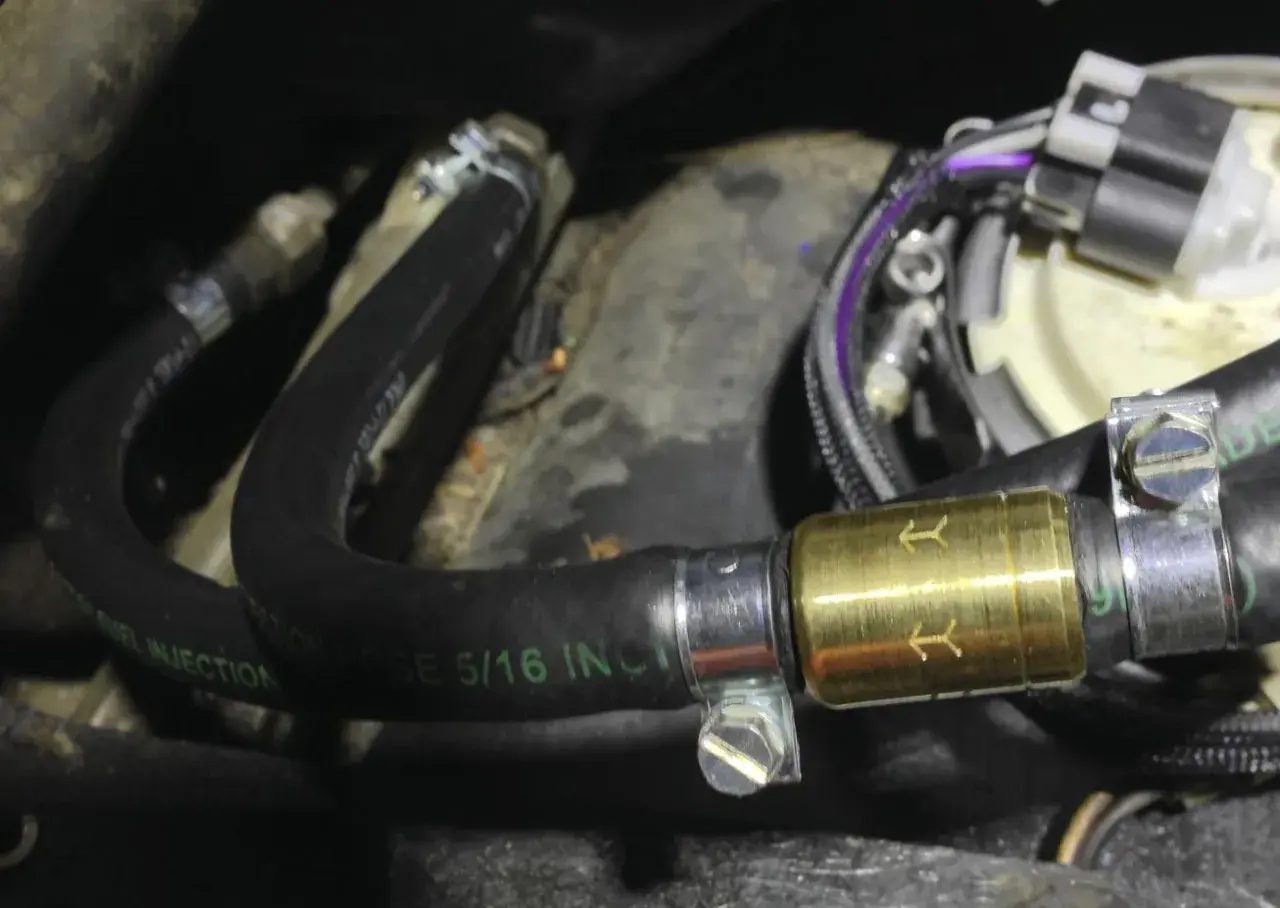 Złoty zawór zwrotny paliwa zamontowany na czarnym wężu paliwowym z oznaczeniem "FUEL INJECTION".