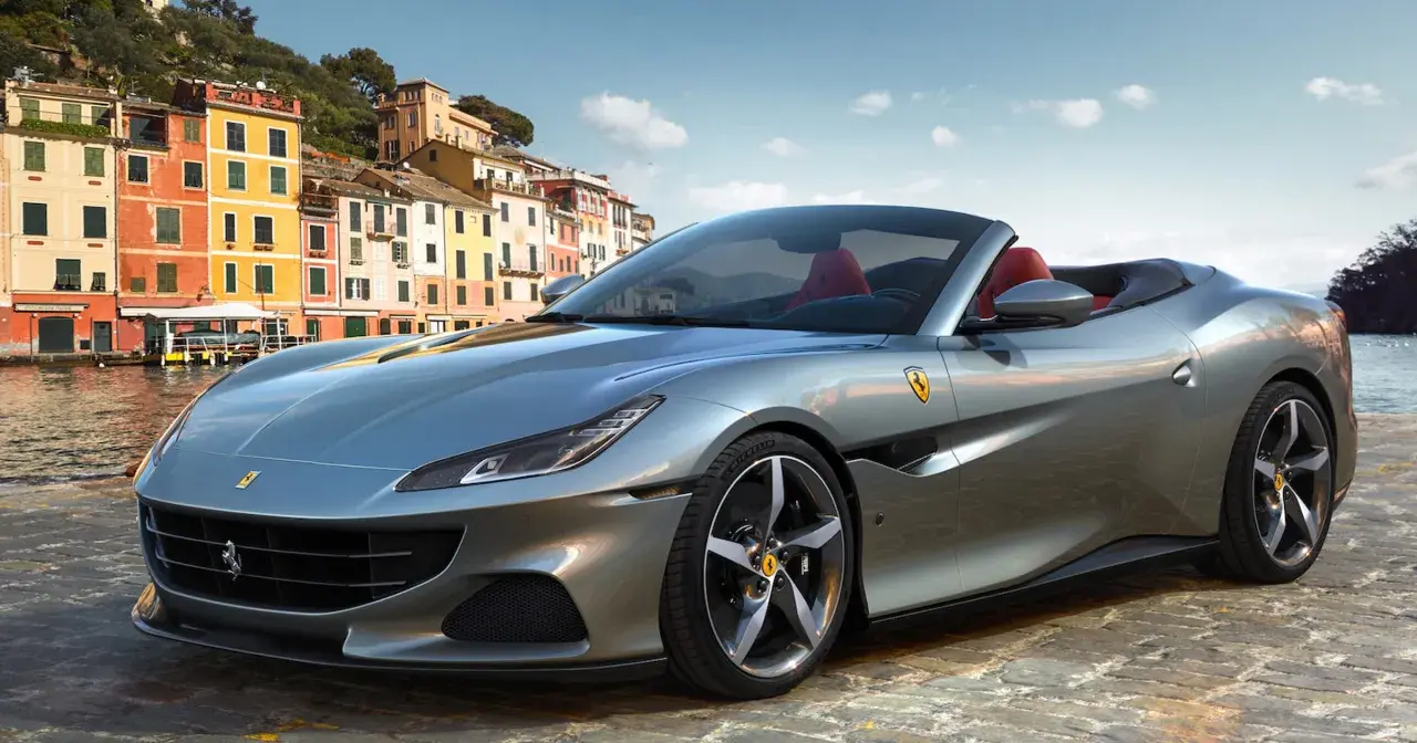 Srebrny Ferrari Portofino z czerwonym wnętrzem na tle kolorowych budynków nad wodą.