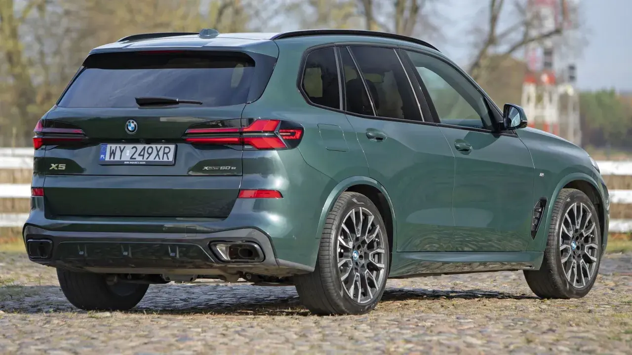 Zielony x5 BMW z napisem XDrive 50e na klapie bagażnika, zaparkowany na bruku.