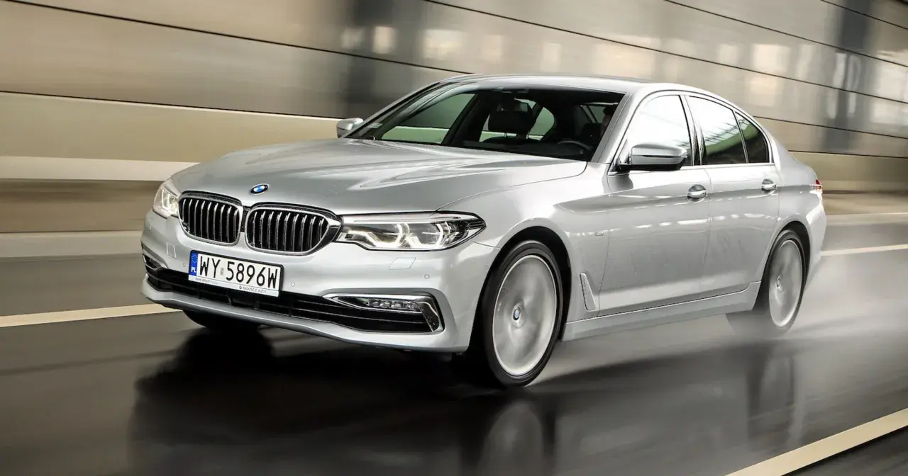 Srebrne BMW 520d xDrive pędzi po mokrej drodze w tunelu, rozpryskując wodę.