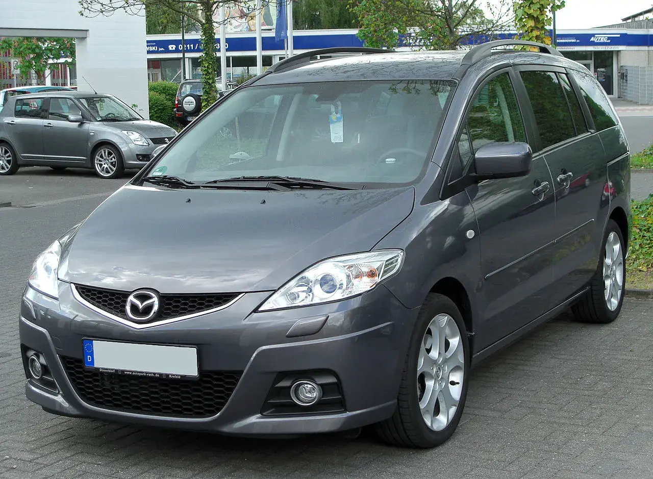 Szary Mazda Premacy stoi na parkingu. W tle widać inne samochody i budynki.