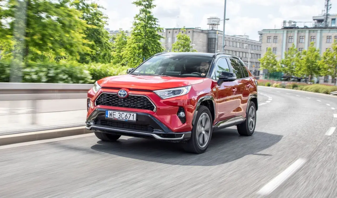 Czerwony Toyota RAV4 2024 na zakręcie drogi, z kierowcą za kierownicą.
