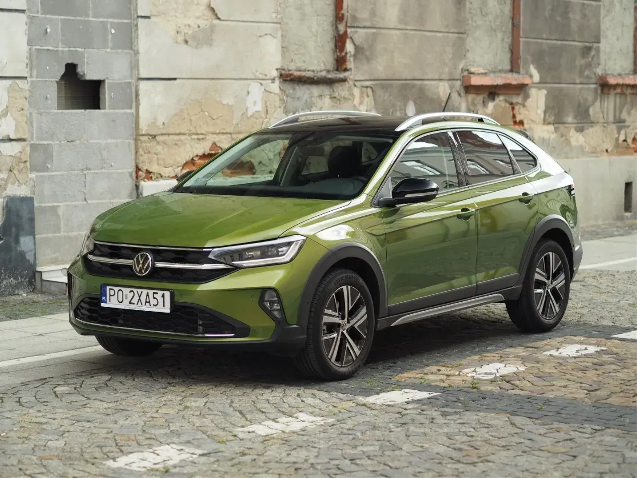 Zielony Volkswagen Taigo na brukowanej ulicy, z charakterystycznym dachem i felgami.