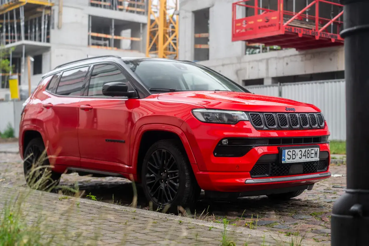 Czerwony Jeep Compass na tle budowy. Wiele osób szuka jeep compass opinie przed zakupem.