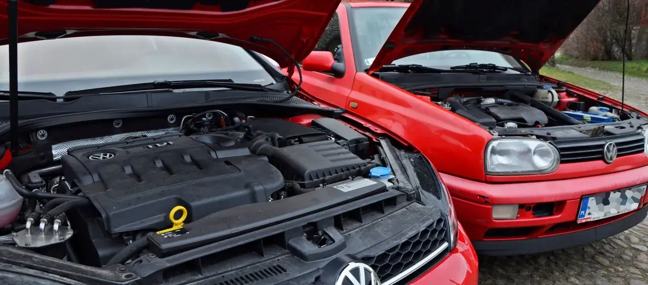 Dwa czerwone Volkswageny z otwartymi maskami. Widać silnik TDI, czyli silnik diesla, w nowszym modelu i starszy silnik w Golfie III.