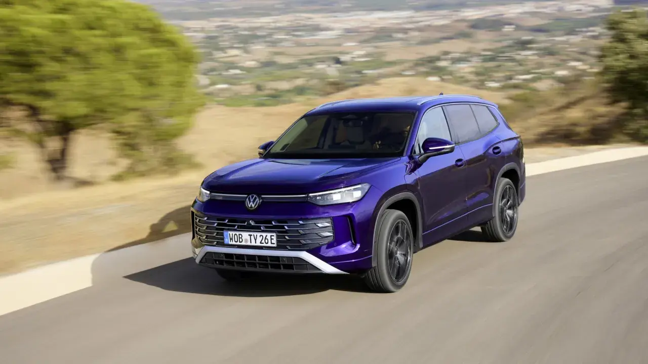 Fioletowy VW Tayron jedzie po krętej drodze wśród wzgórz.