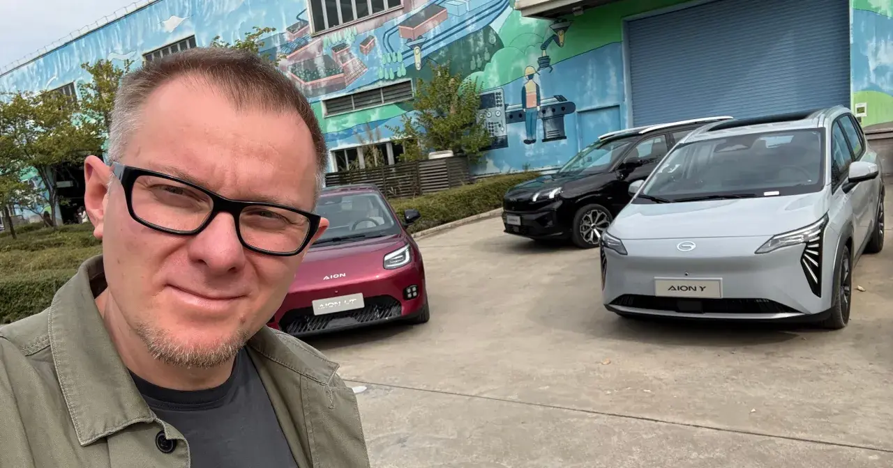 Mężczyzna w okularach pozuje do selfie na tle trzech samochodów marki AION.