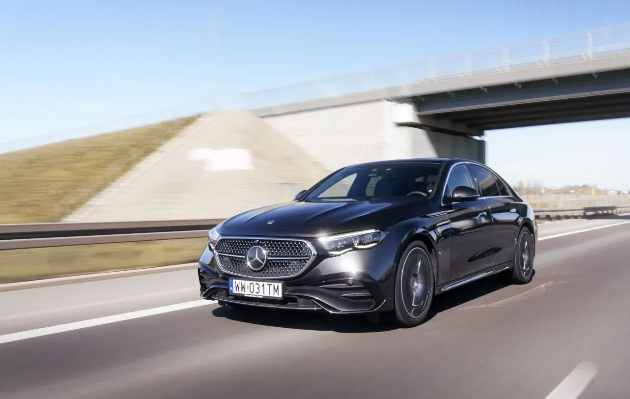 Czarny Mercedes E220d pędzi autostradą pod mostem.