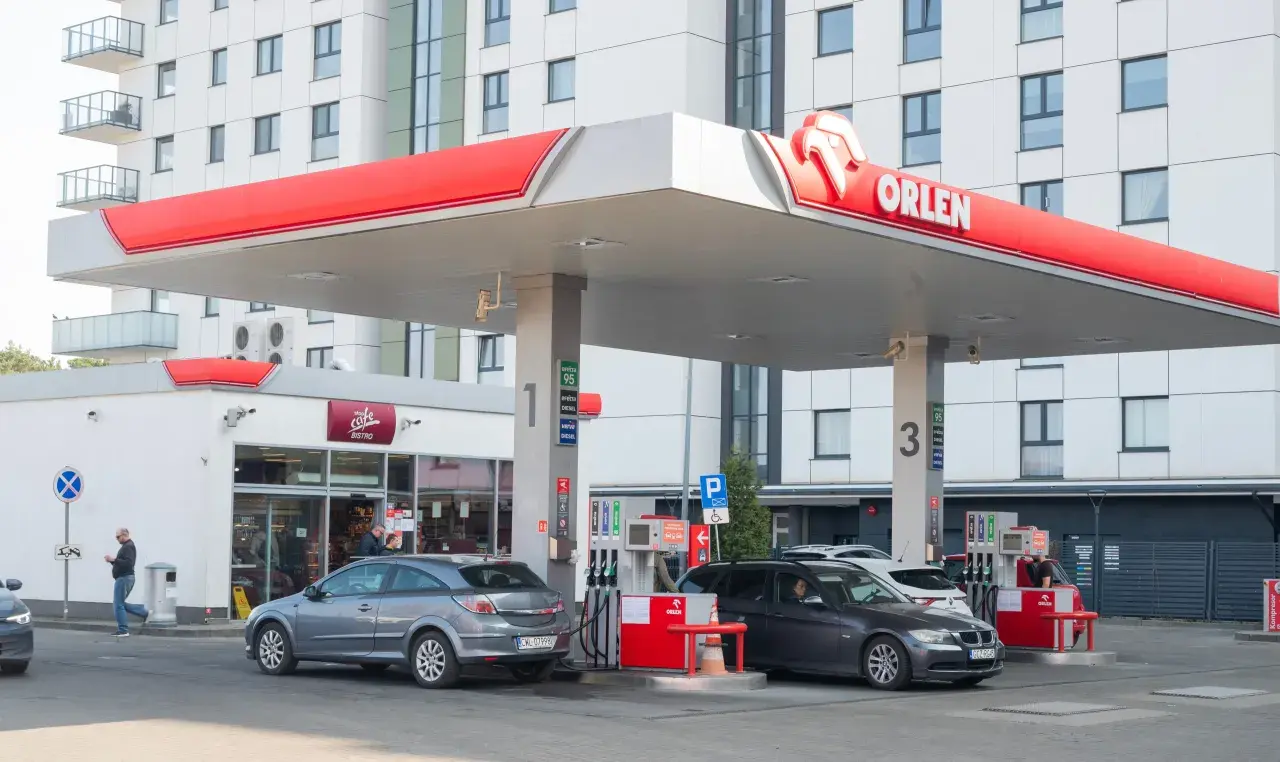 Stacja Orlen z dystrybutorami paliwa. W tle nowoczesny budynek mieszkalny. Ceny paliw, w tym akcyza, wpływają na koszty tankowania.