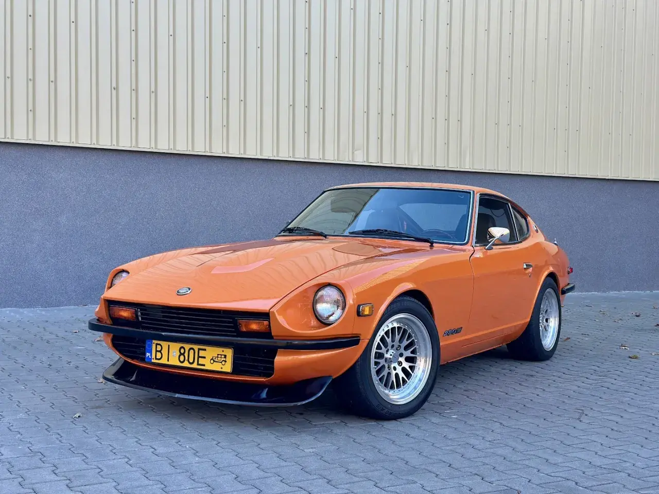 Pomarańczowy Datsun 280Z z lat 70. na tle budynku. Klasyk motoryzacji gotowy na przejażdżkę.