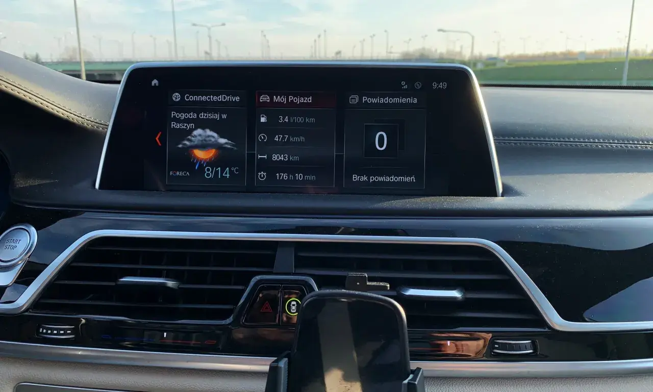 Wnętrze BMW hybryda: ekran z pogodą w Raszynie (8/14°C), spalaniem 3.4l/100km i przebiegiem 8043km.