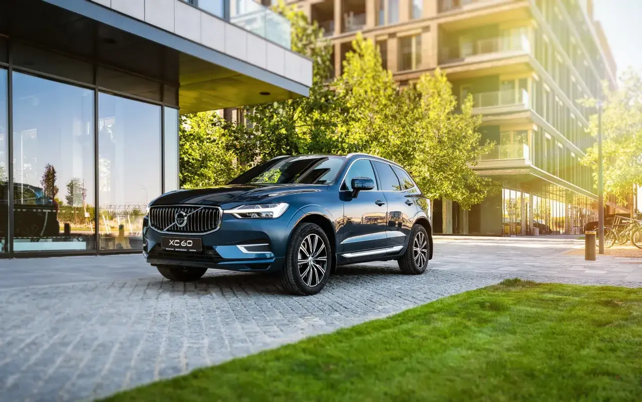 Elegancki, ciemnoniebieski Volvo XC60 zaparkowany przed nowoczesnym budynkiem. Wiele osób szuka volvo xc60 opinie, by podjąć decyzję o zakupie.